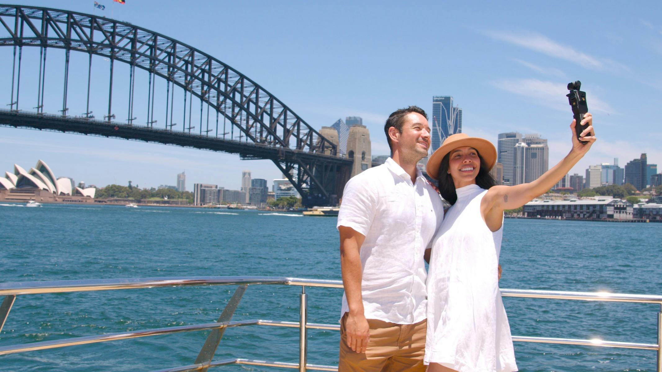 couple on a cruise taking a selfie in front of the Sydney Harbour Bridge