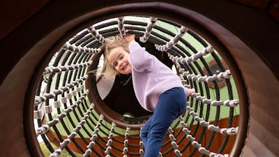 Young girl smiling at camera as she climbs through a net tunnel