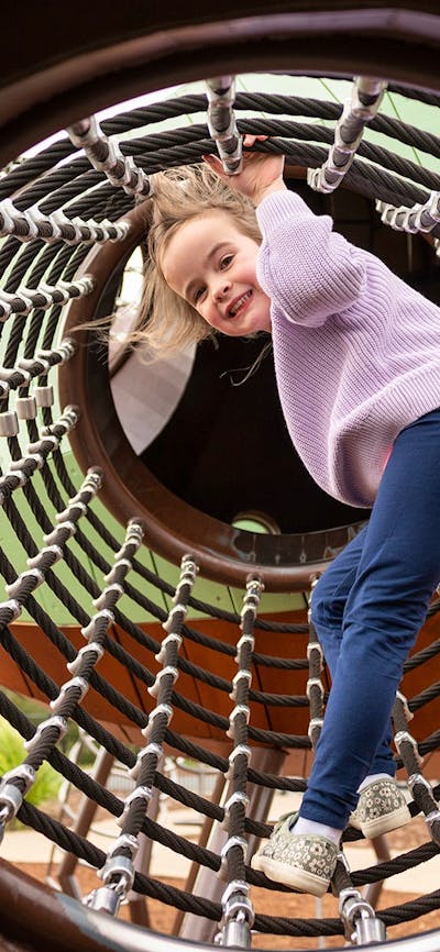 Young girl smiling at camera as she climbs through a net tunnel