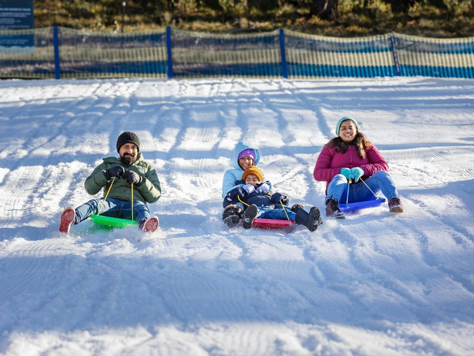 A family of four smiles as they race down a snowy slope on colourful toboggans