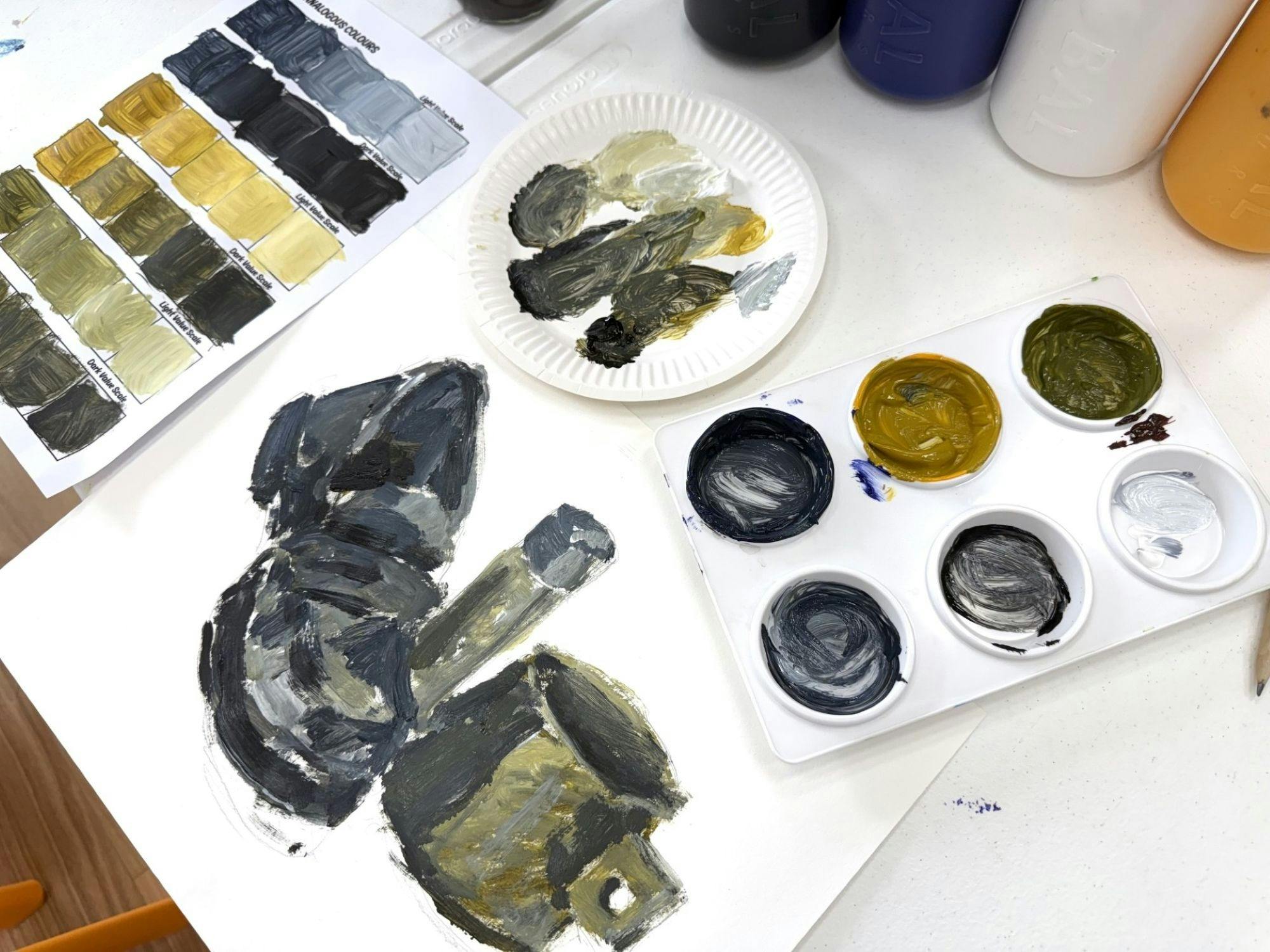 Art materials laid out on table showing a colour scale, paint palette and a painting in progress