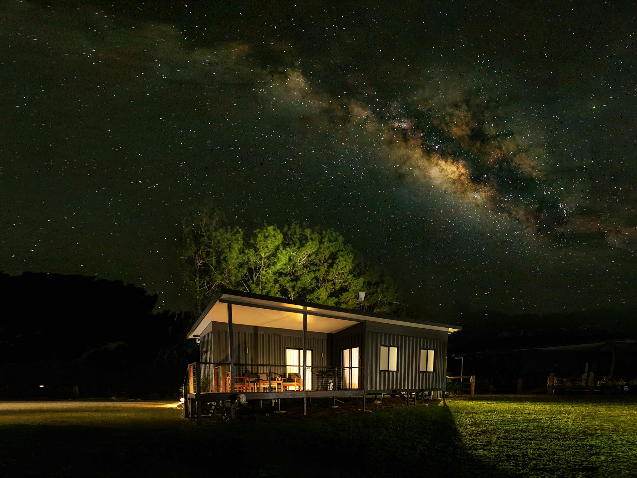 An image of Wollumbin cottage sitting in a paddock at night with the Milky Way arching over the top.