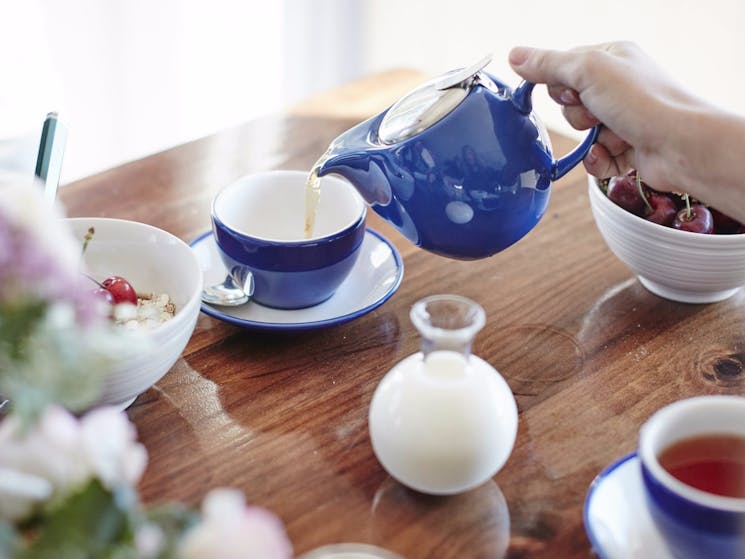 Breakfast with blue teapot and blue cup, cherries in a bowl and cereal in a bowl