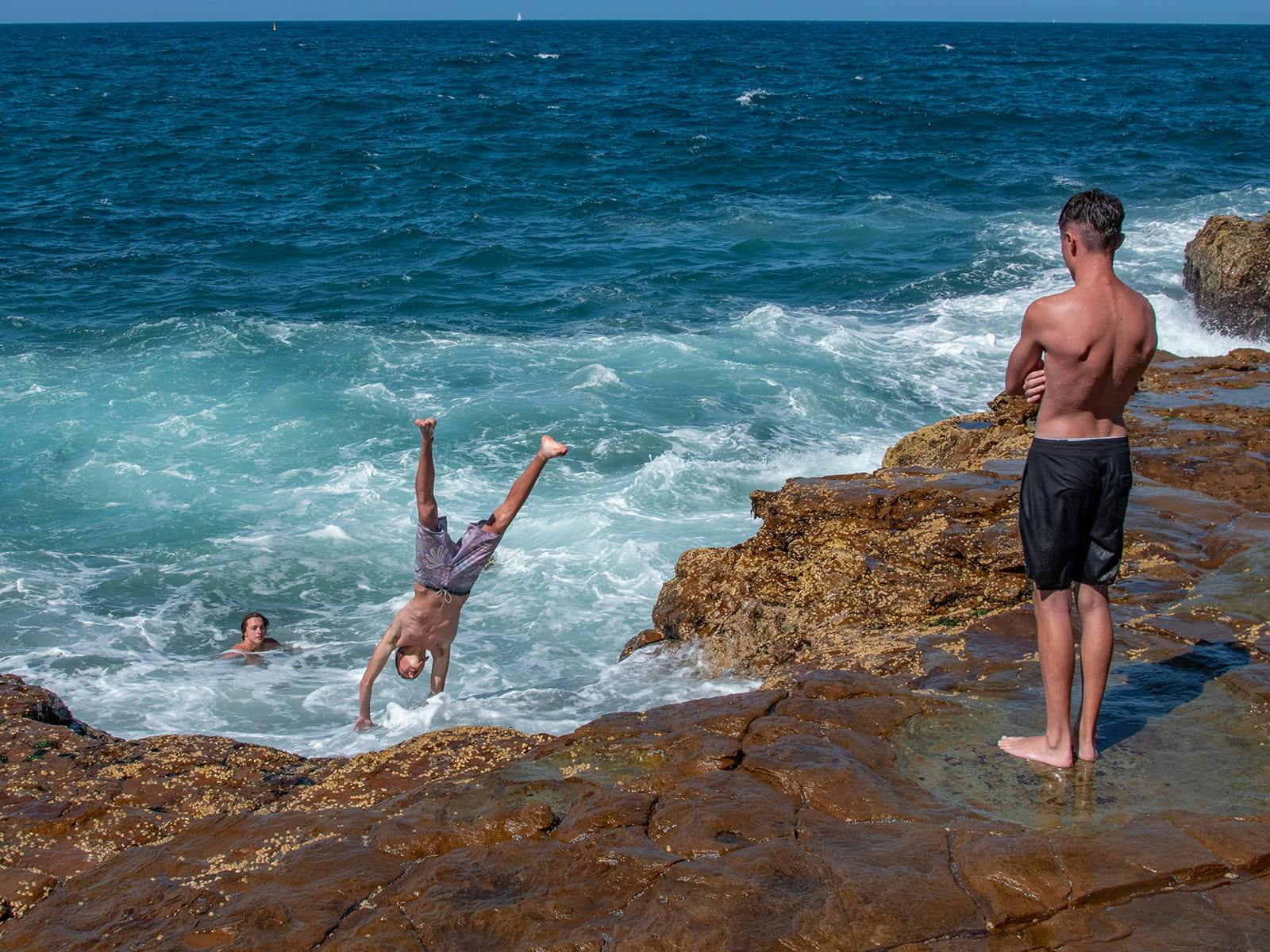 People jumping into ocean waves from rocky coastal cliffs near Sydney.