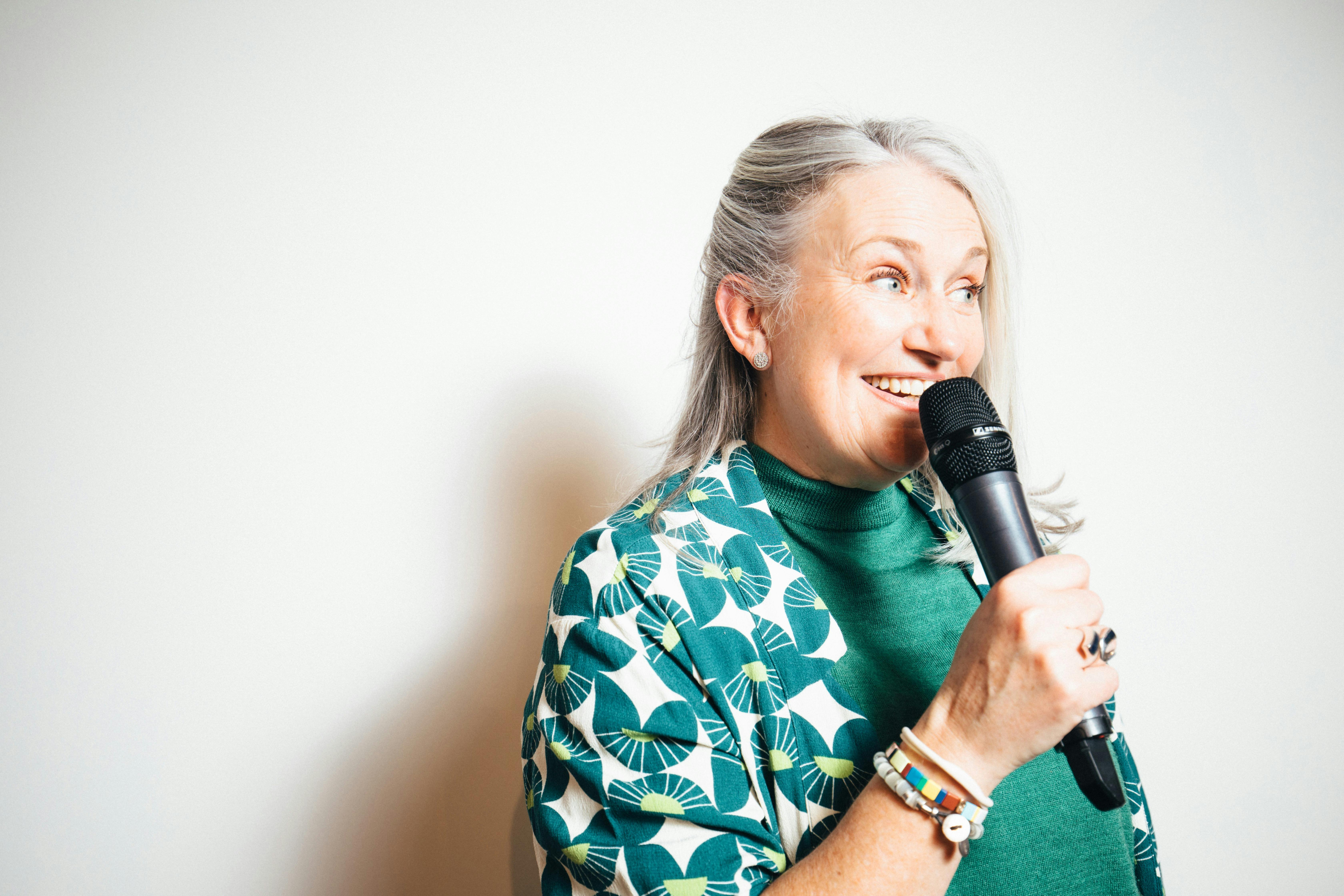 Lady with grey hair and a green outfit holding a microphone