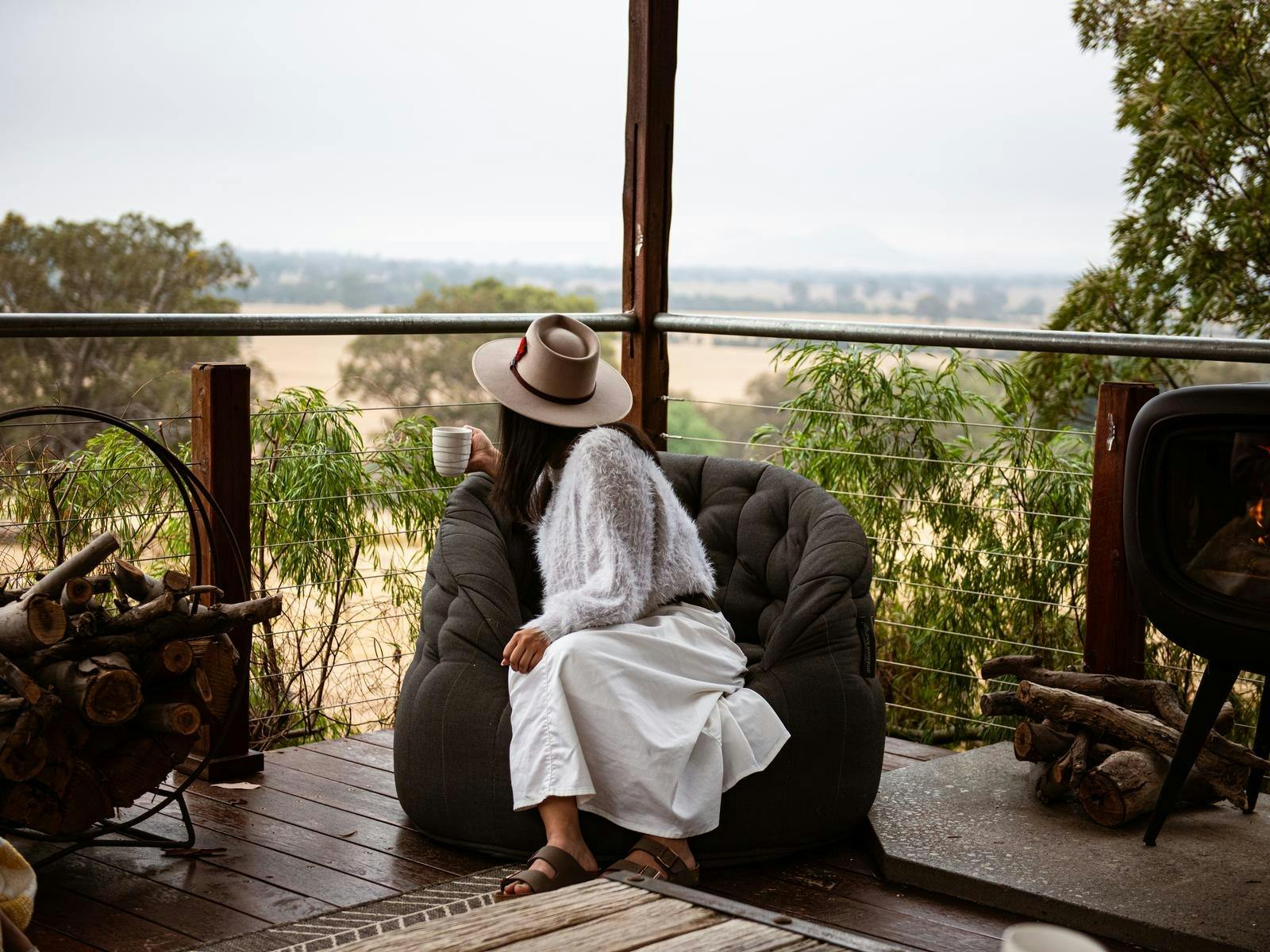 A lady sitting in an oversize lounge pod, next to an outside fireplace looking at view at BullerRoo
