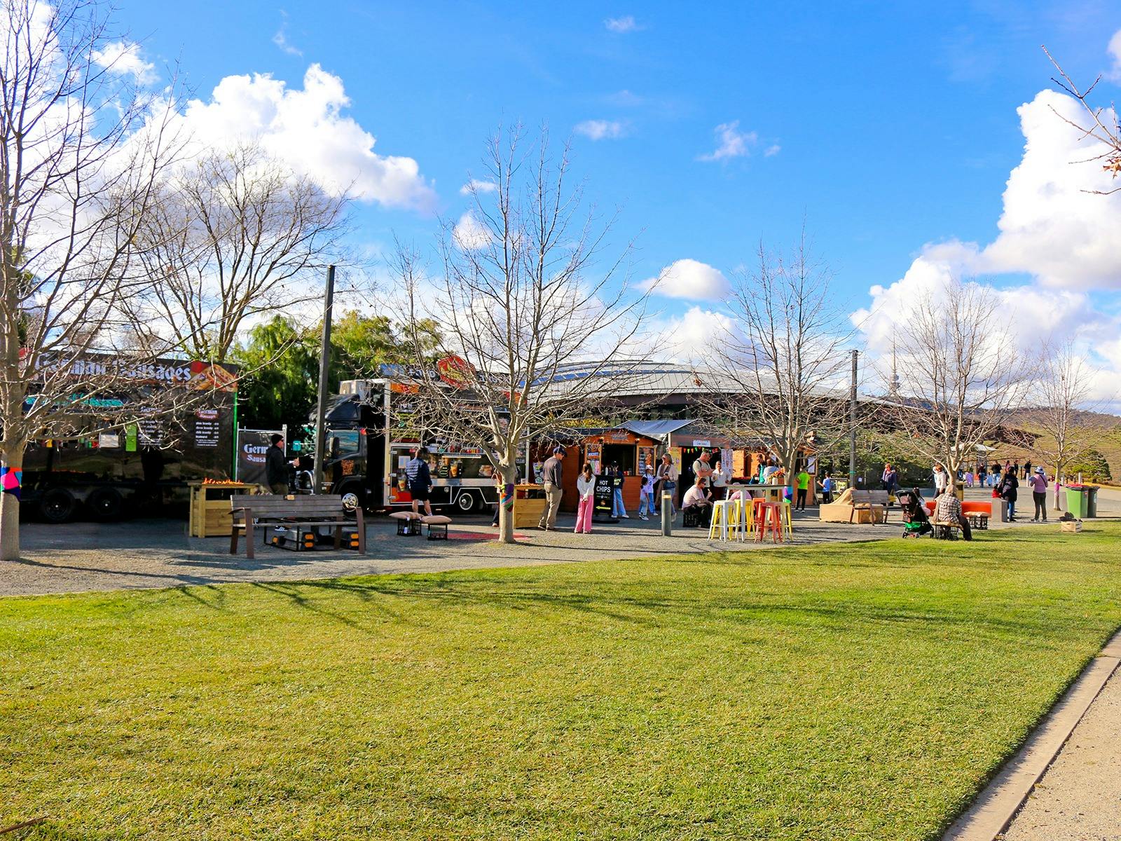 A landscape image shows a row of food vans and vendor stalls with lots of people of all ages