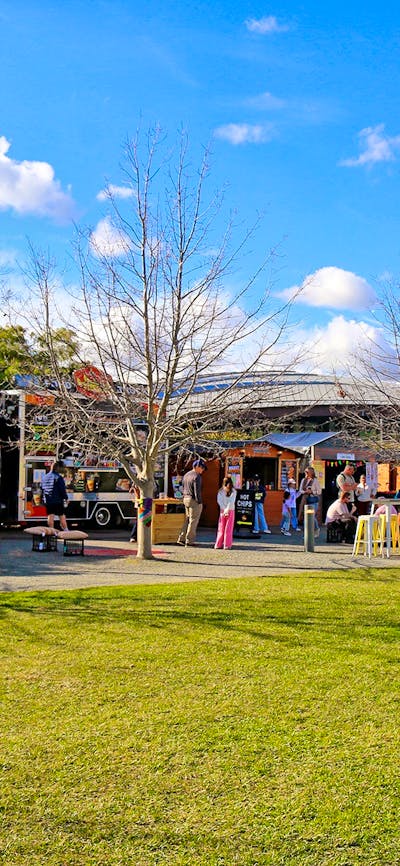 A landscape image shows a row of food vans and vendor stalls with lots of people of all ages