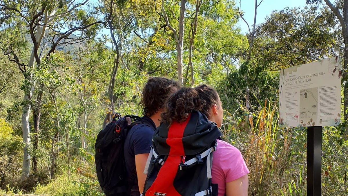 Two people with pack backs standing looking at a sign.