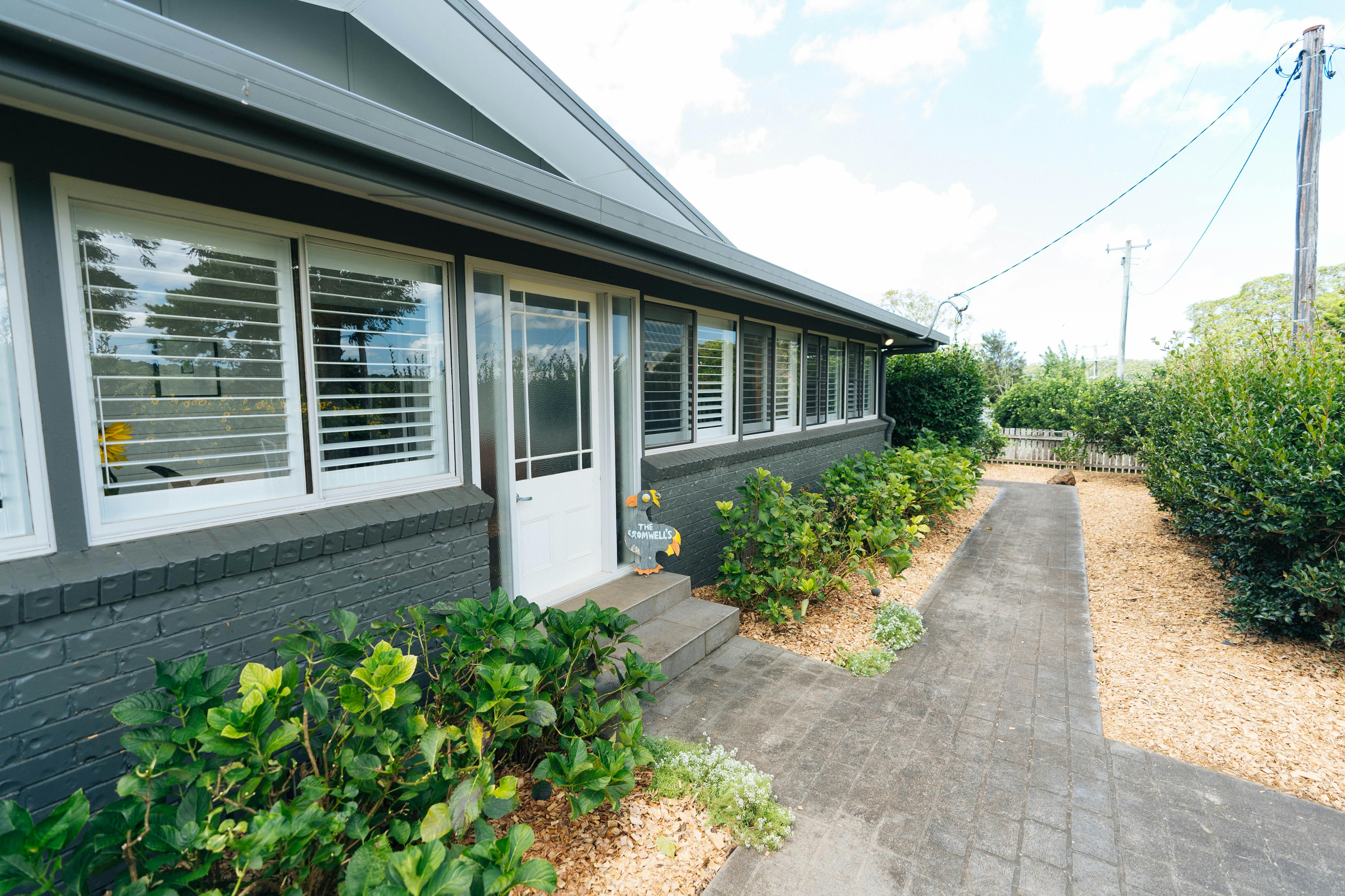 A farm style house with a white front door and plants on either side of the door and a grey path