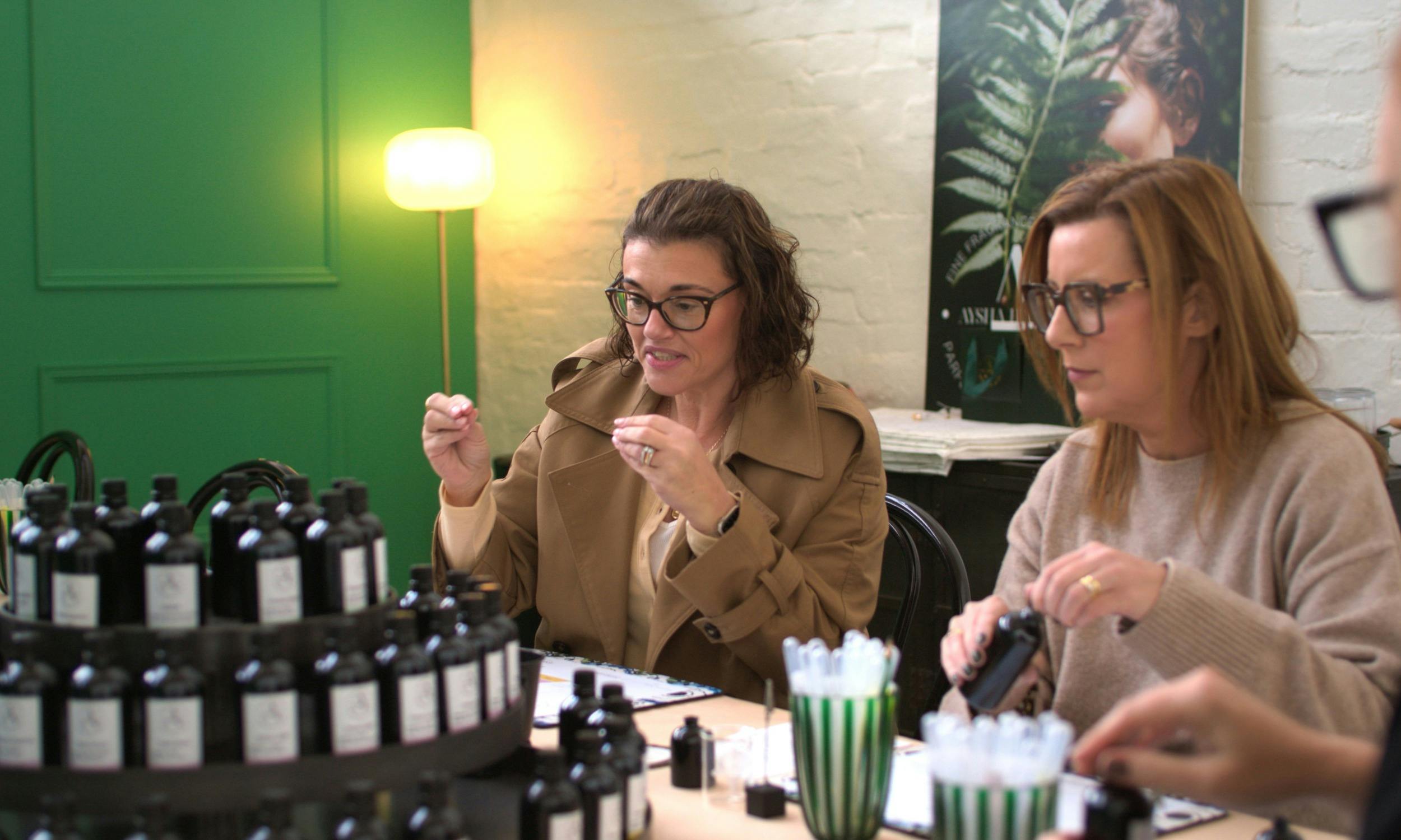 Two women sampling fragrance notes at a perfume workshop while smiling and chatting.