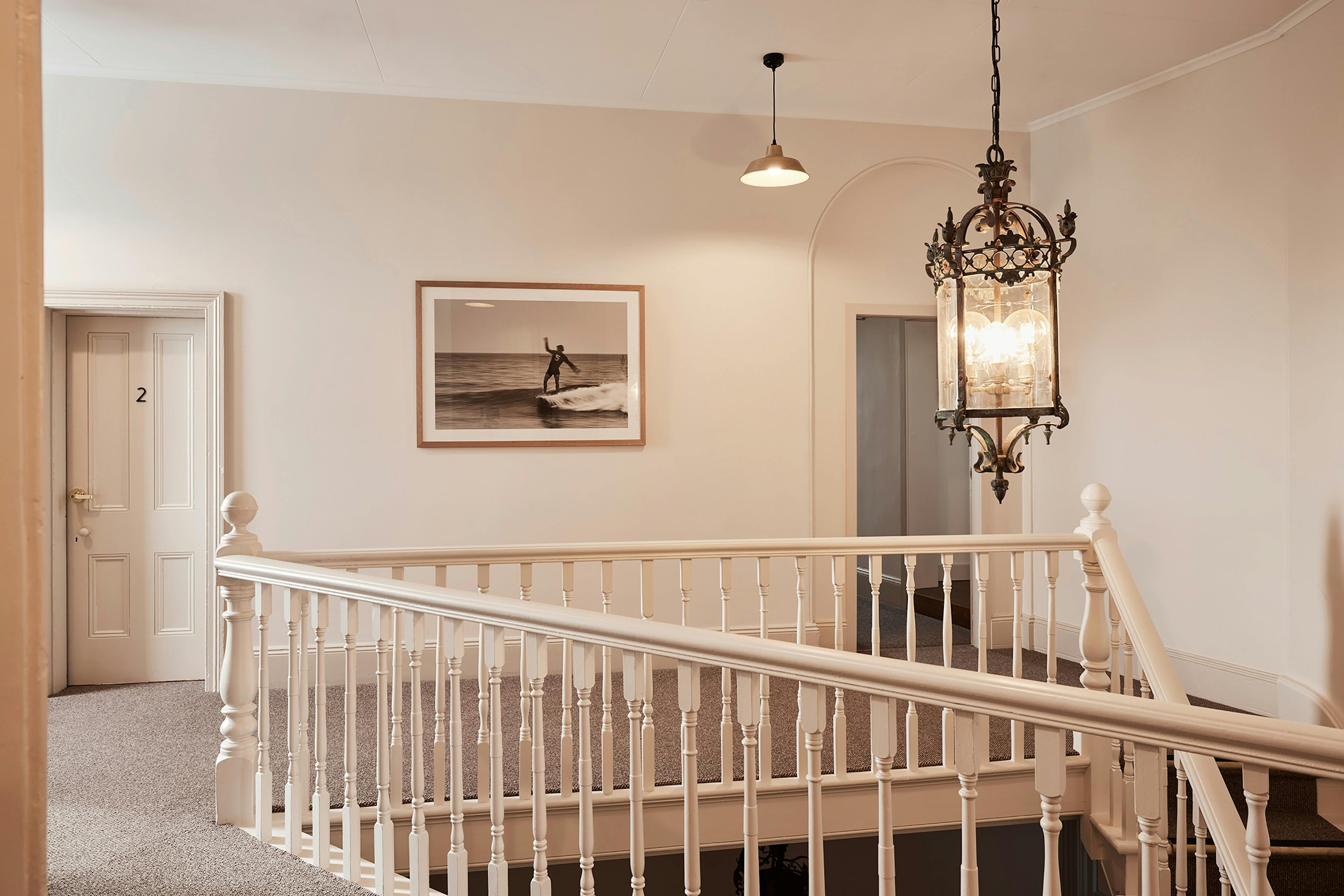 Elegant hallway with white balustrade, vintage chandelier, and surf-themed artwork