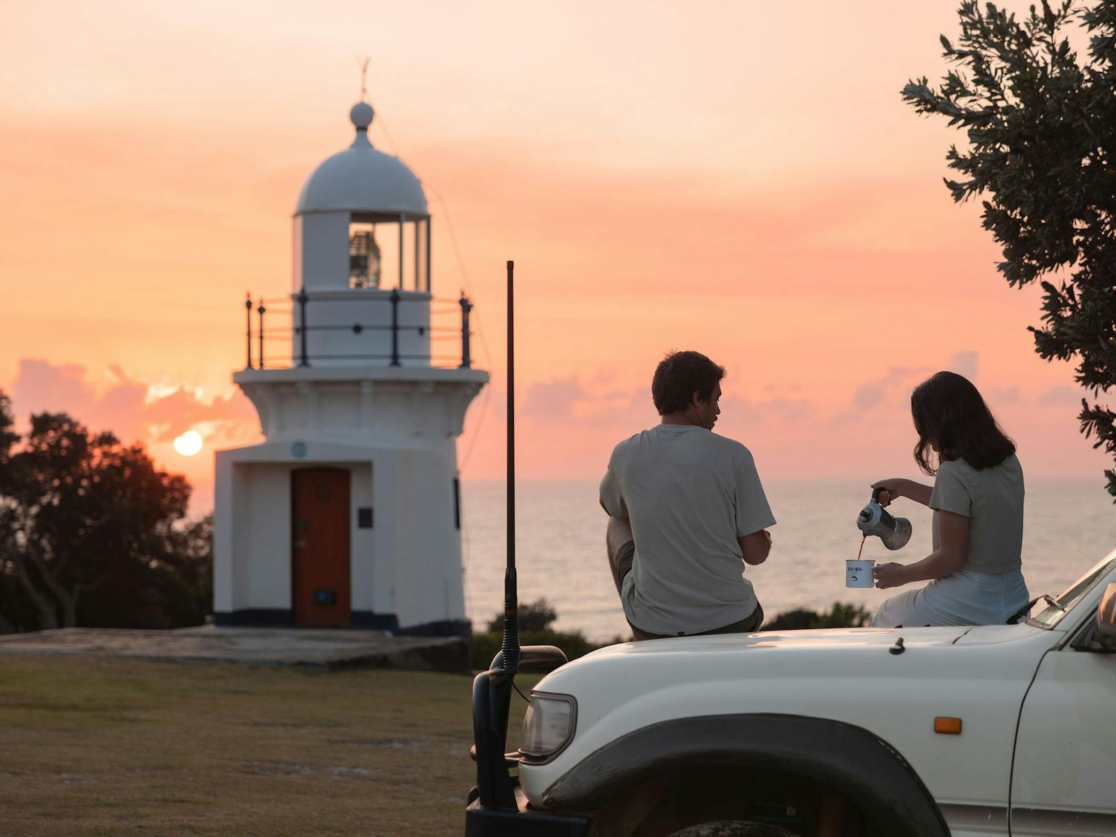 Sunset shot of the lighthouse with a couple drinking coffee on their car