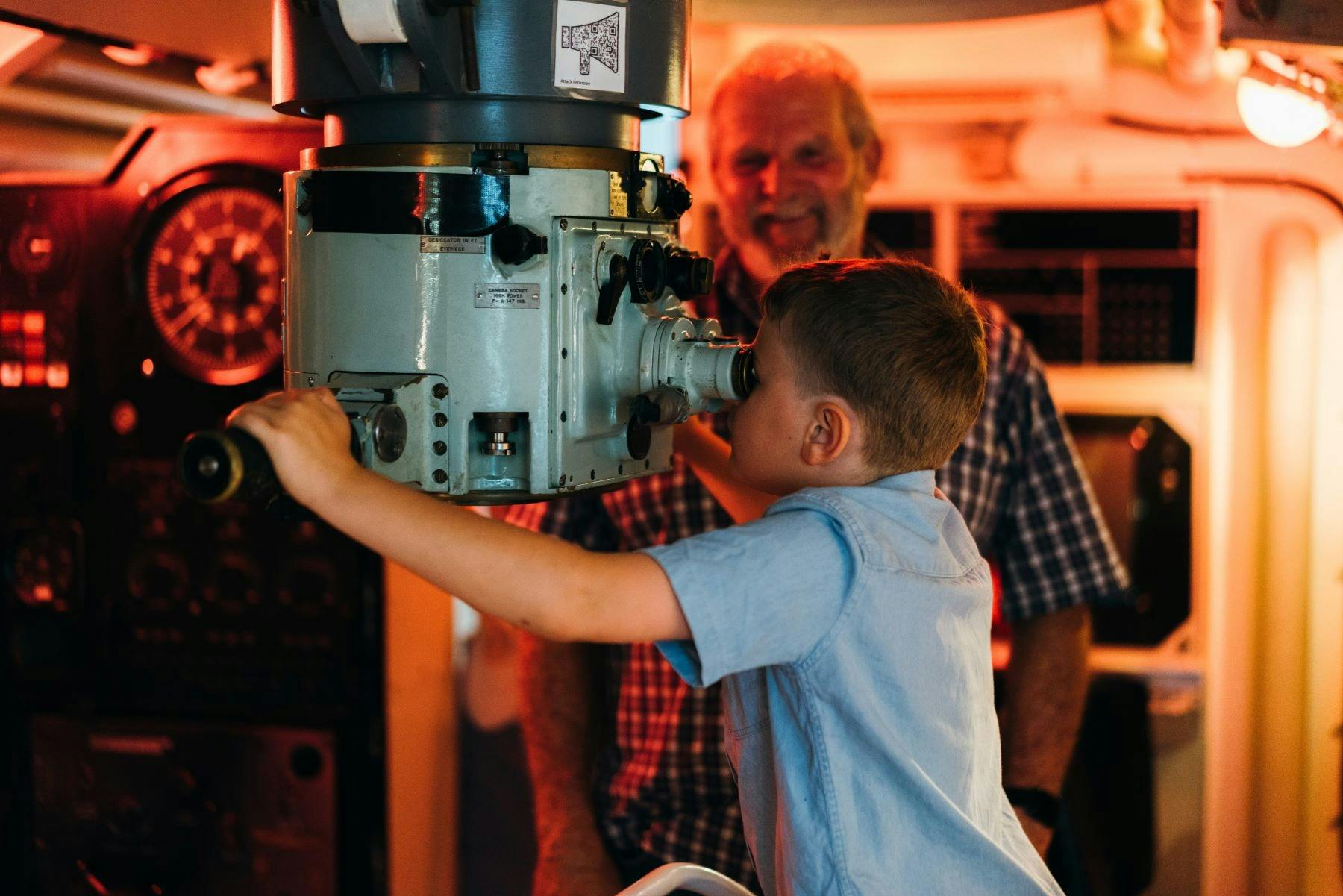 Boy looking through working periscope while grandfather looks on