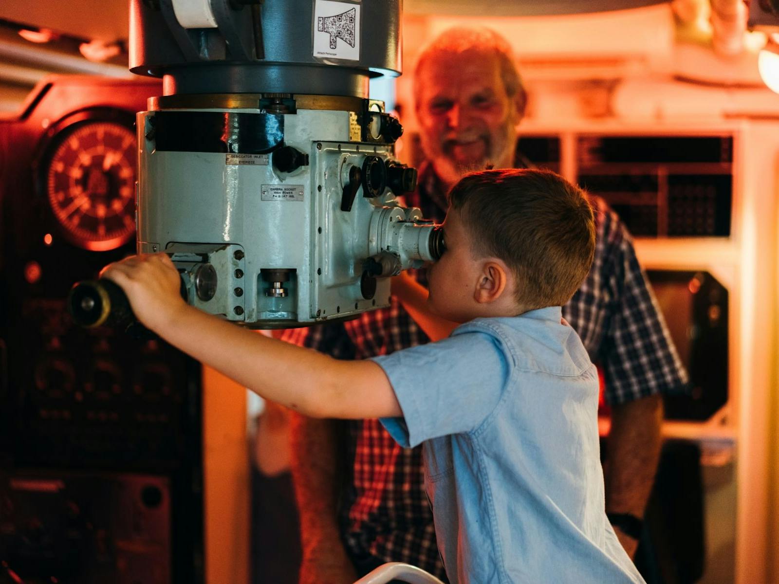 Boy looking through working periscope while grandfather looks on