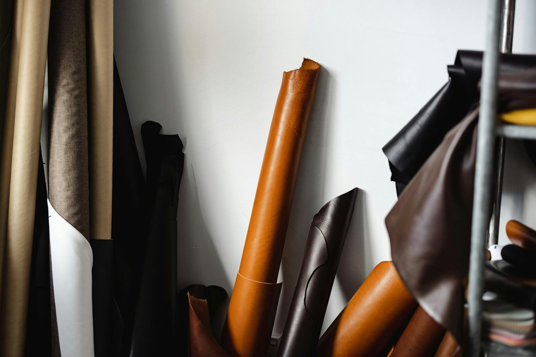 Rolled leather hides in tan, brown, and black, stacked against a wall in a leather workshop