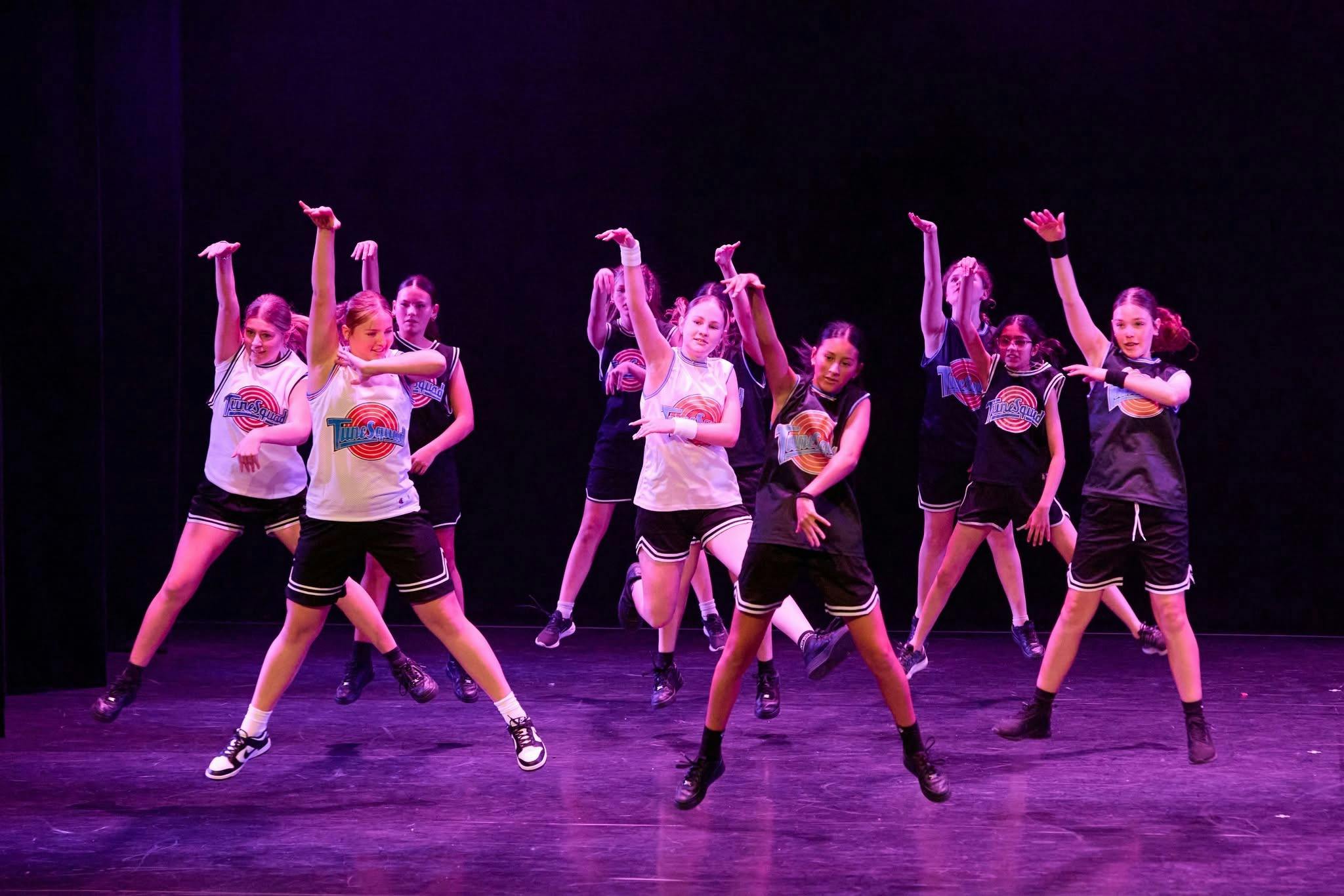 A group of young dancers performing a synchronized routine, wearing basketball inspired costumes.