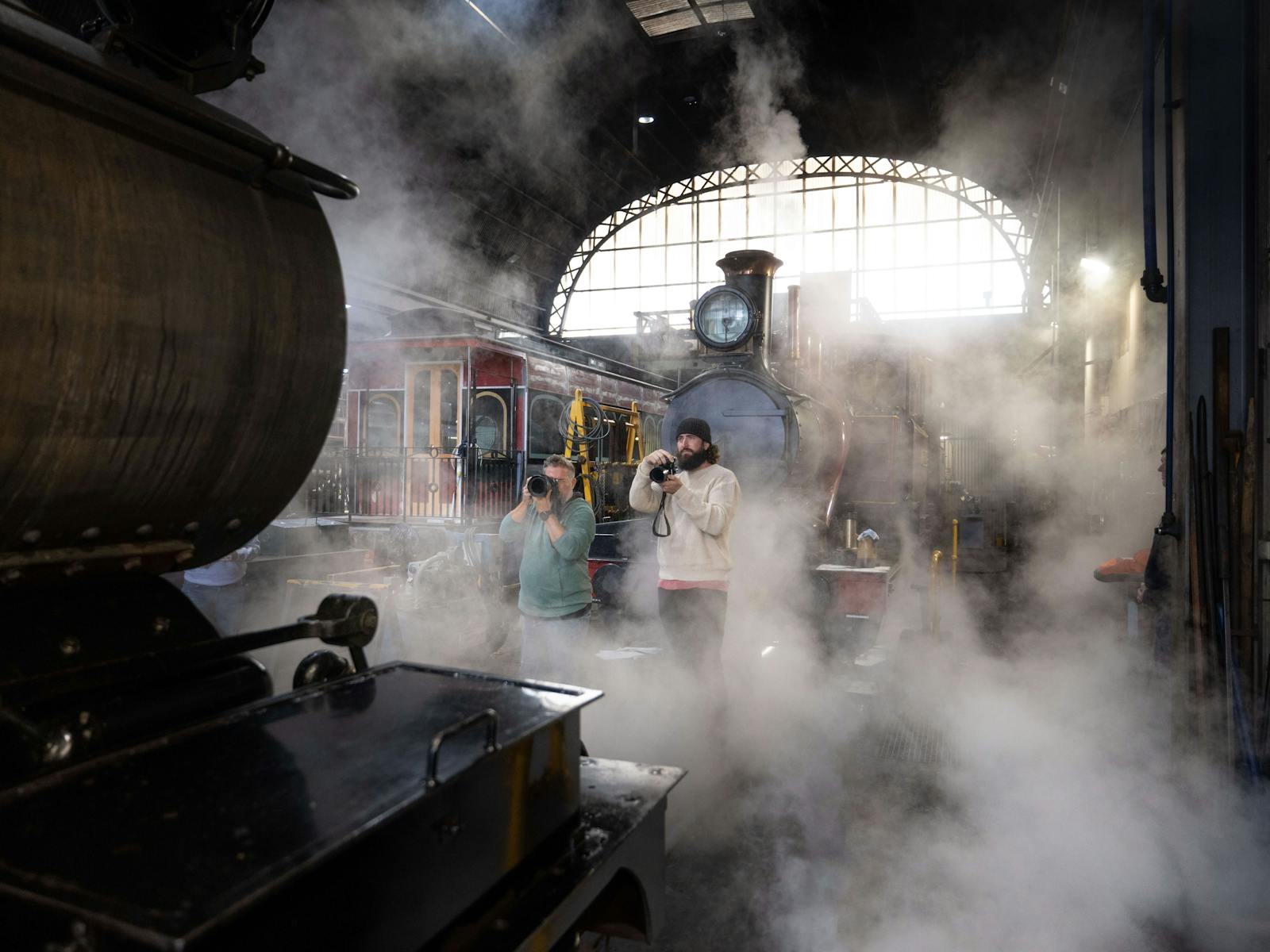 Two photographers face a steaming locomotive with a second loco behind them