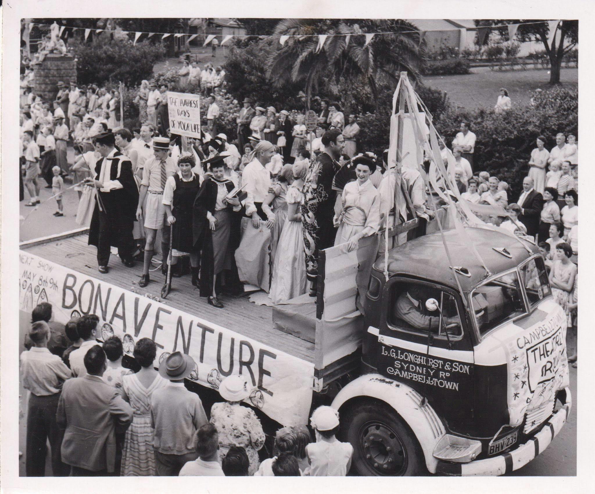 An old image of a parade with people on the back of a truck in fancy dress