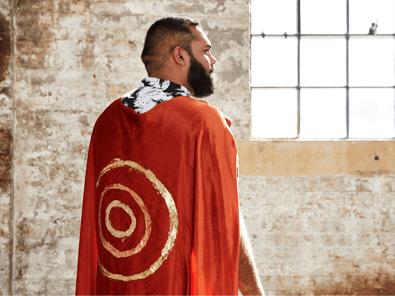 a man turned away from the camera wearing an orange cape with concenttic yellow circles