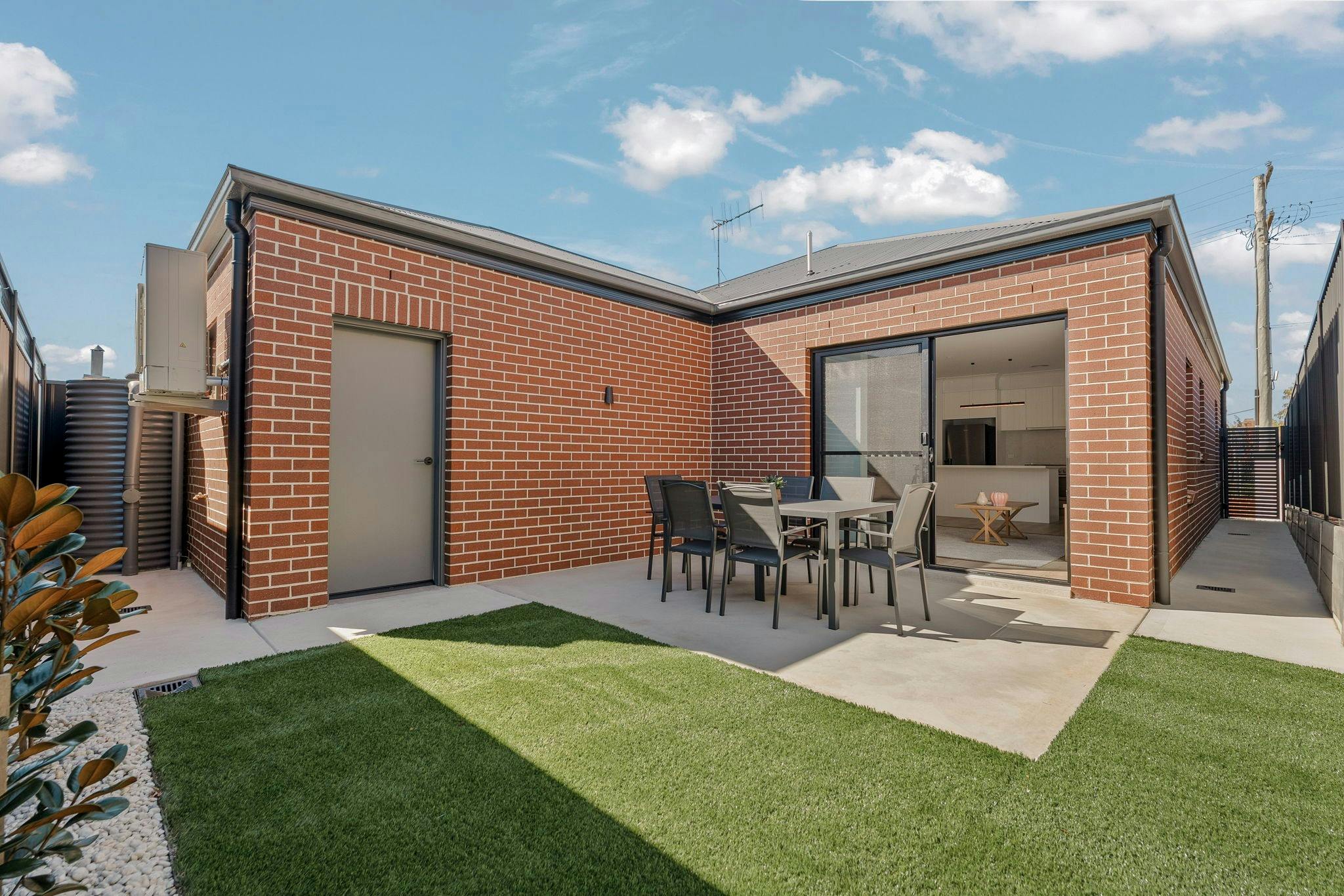 Red brick home with concreted outdoor area for dining table and lovely green grass area.