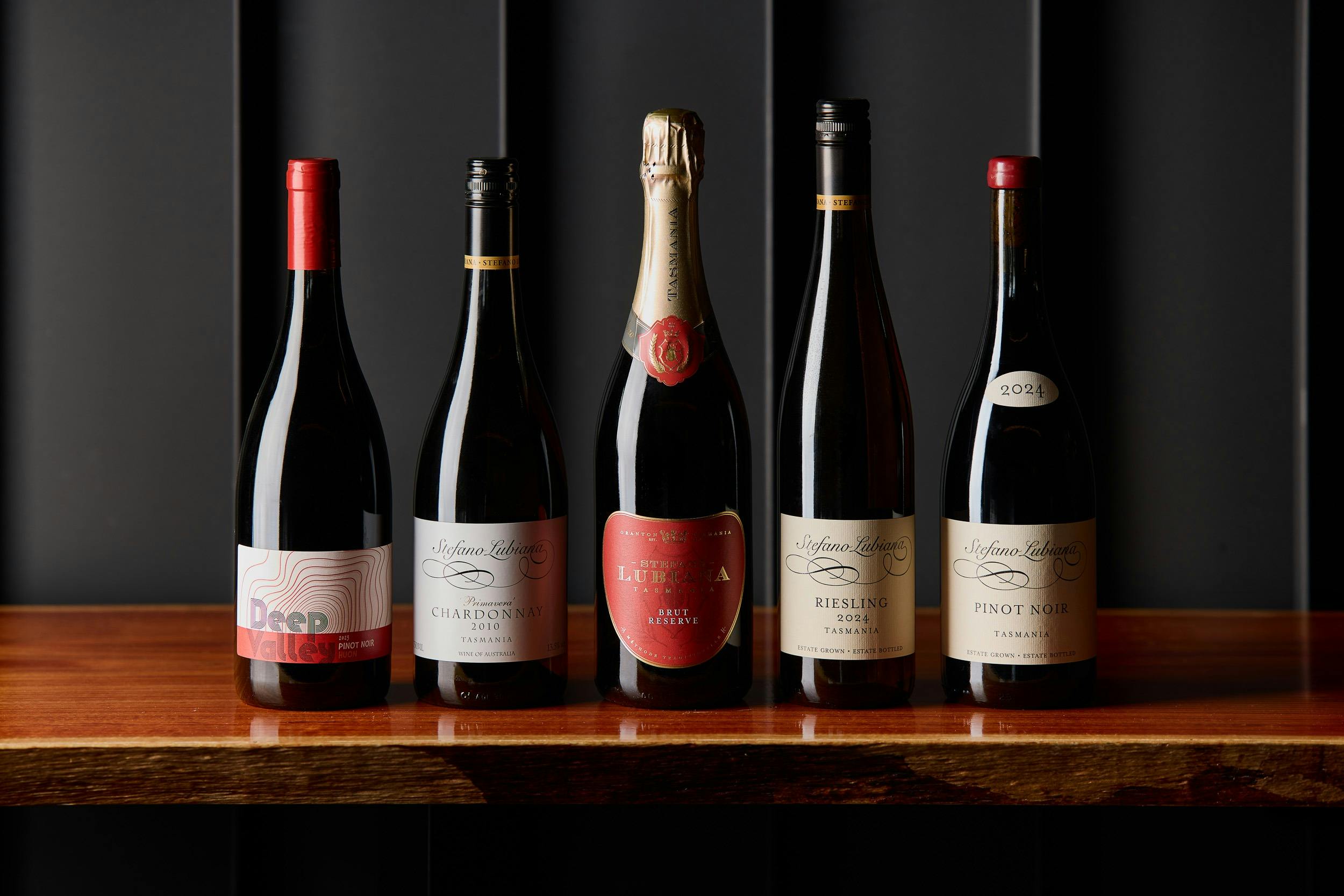 A selection of five Stefano Lubiana wine bottles lined up on a table against a black background
