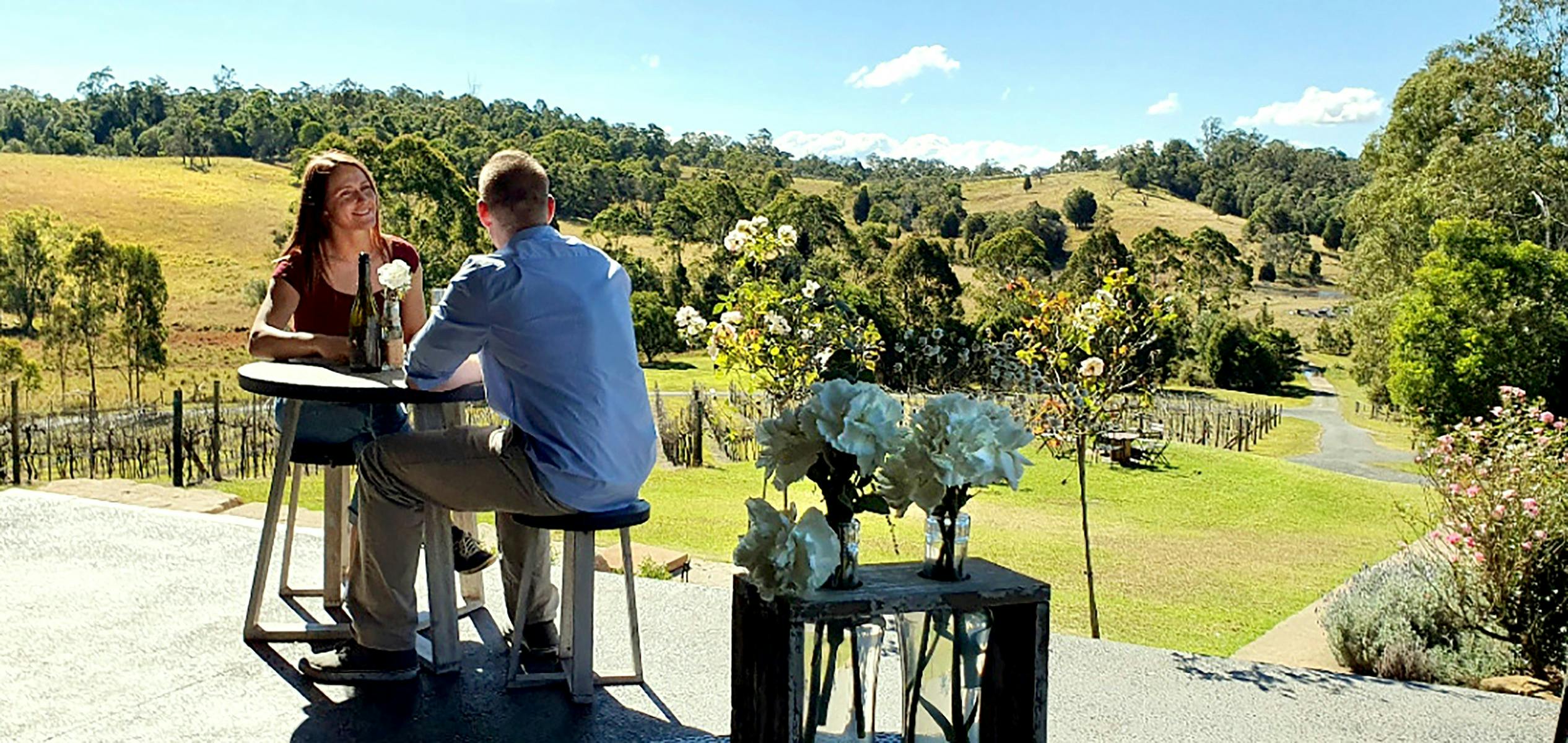 a couple enjoying some wine on a deck overlooking a vineyard