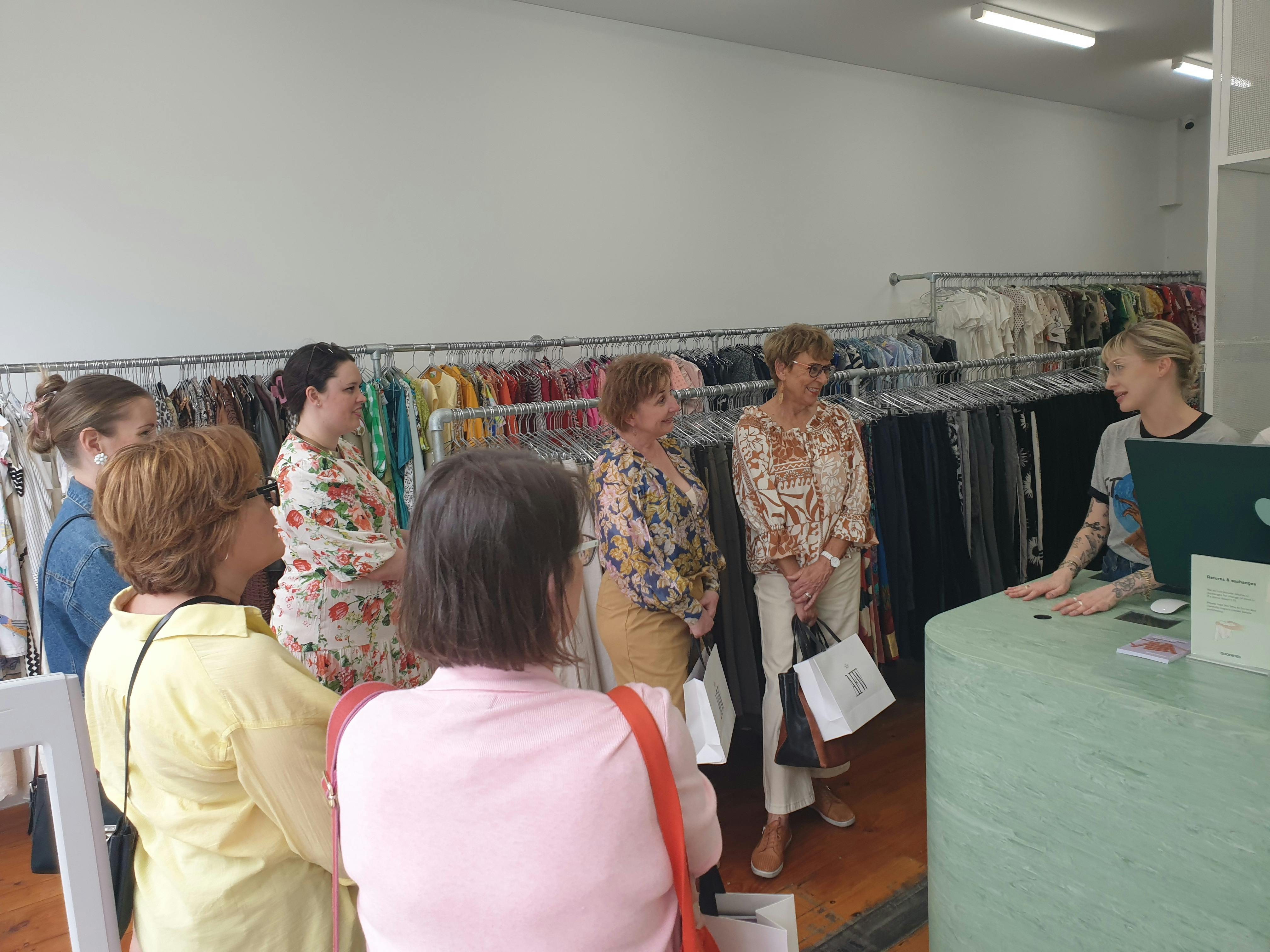 A tour group stands and listens to a staff member explain their store during a shopping tour.