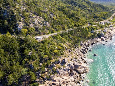 Drone shot of tour bus travelling a mountainside road, overlooking oceans Drone shot of tour bus travelling a mountainside road, overlooking oceans