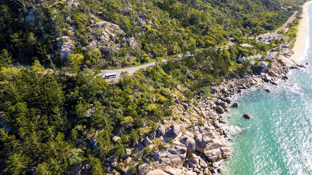 Drone shot of tour bus travelling a mountainside road, overlooking oceans