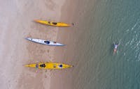 A person floats in crystal clear waters in front of a sandy beach upon which 3 kayaks rest