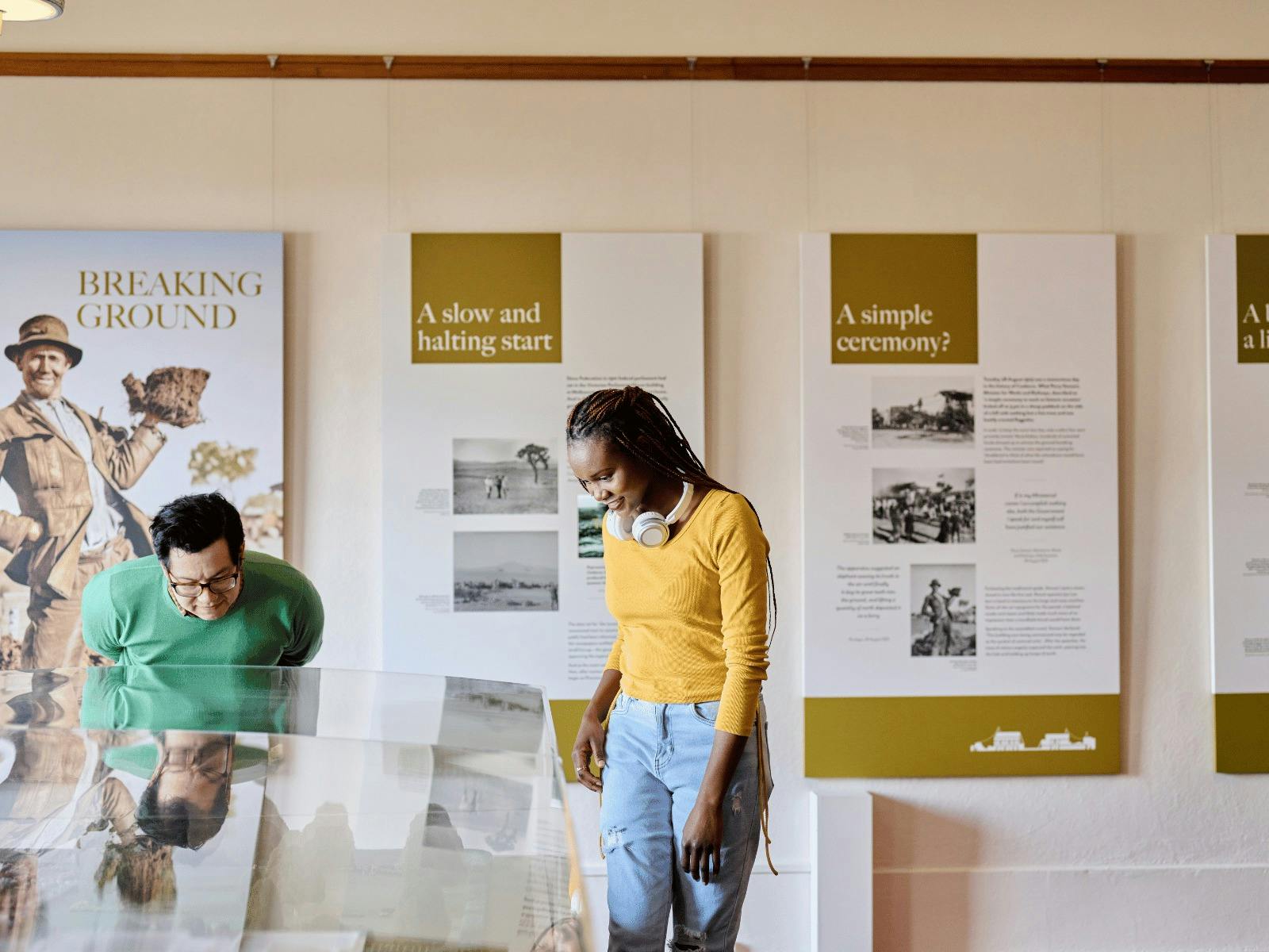 Two people observe a miniature version of Old Parliament House beneath a glass display case