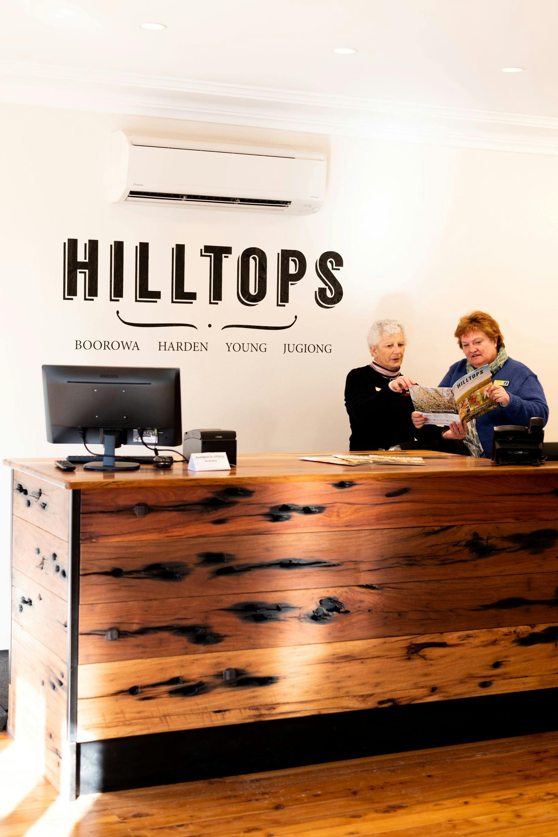 Tourism Officer serving a visitor behind the counter. The logo "HILLTOPS" on the wall.