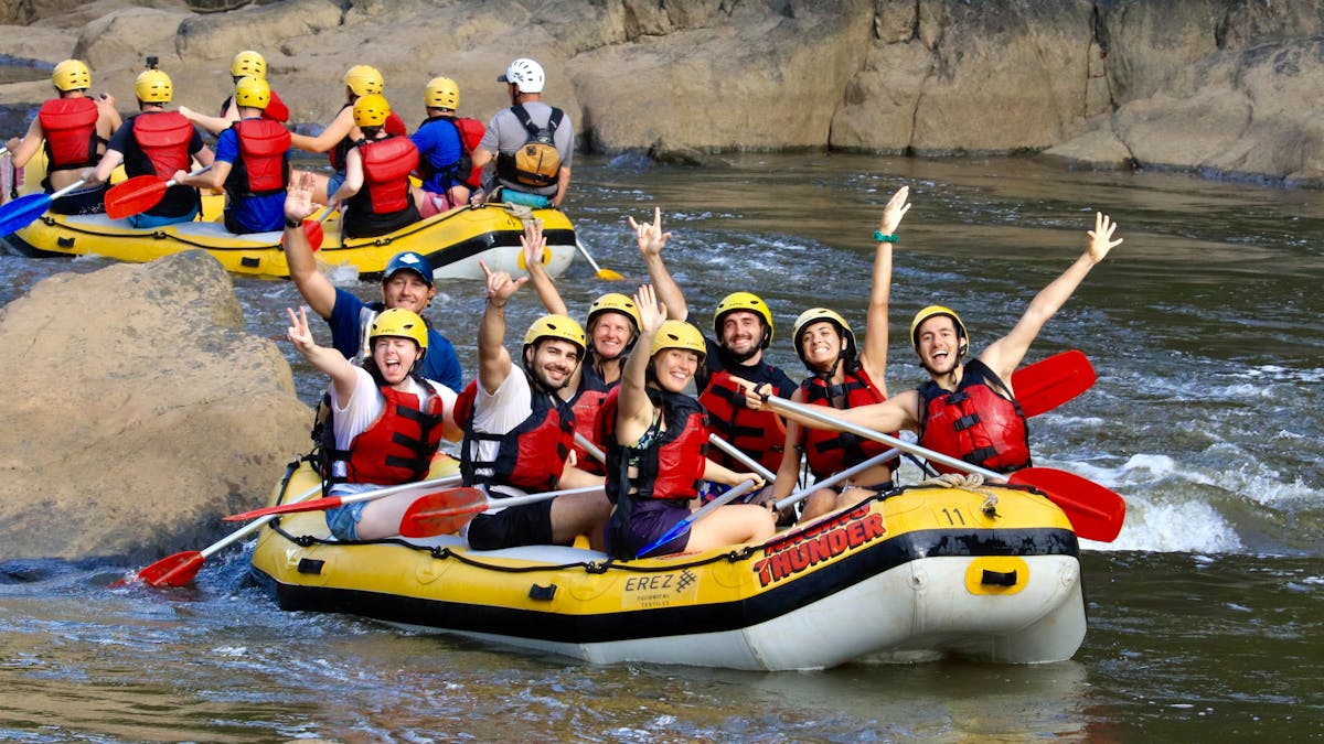 Group of 7 plus guide wave to camera from their raft on the Barron Gorge National Park River