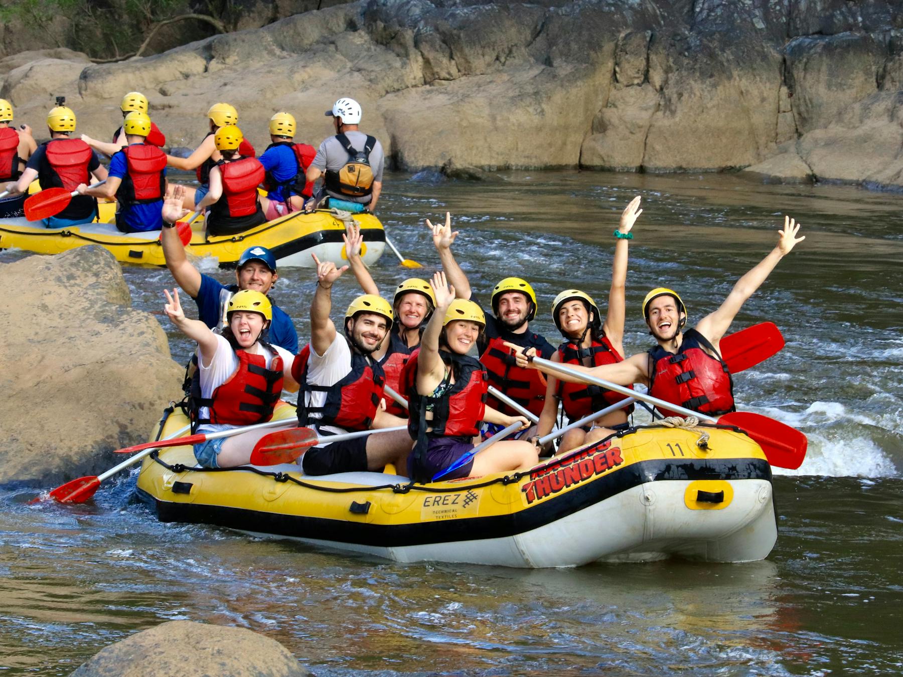 Group of 7 plus guide wave to camera from their raft on the Barron Gorge National Park River