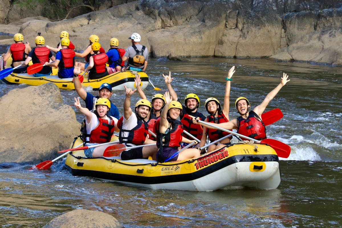 Group of 7 plus guide wave to camera from their raft on the Barron Gorge National Park River