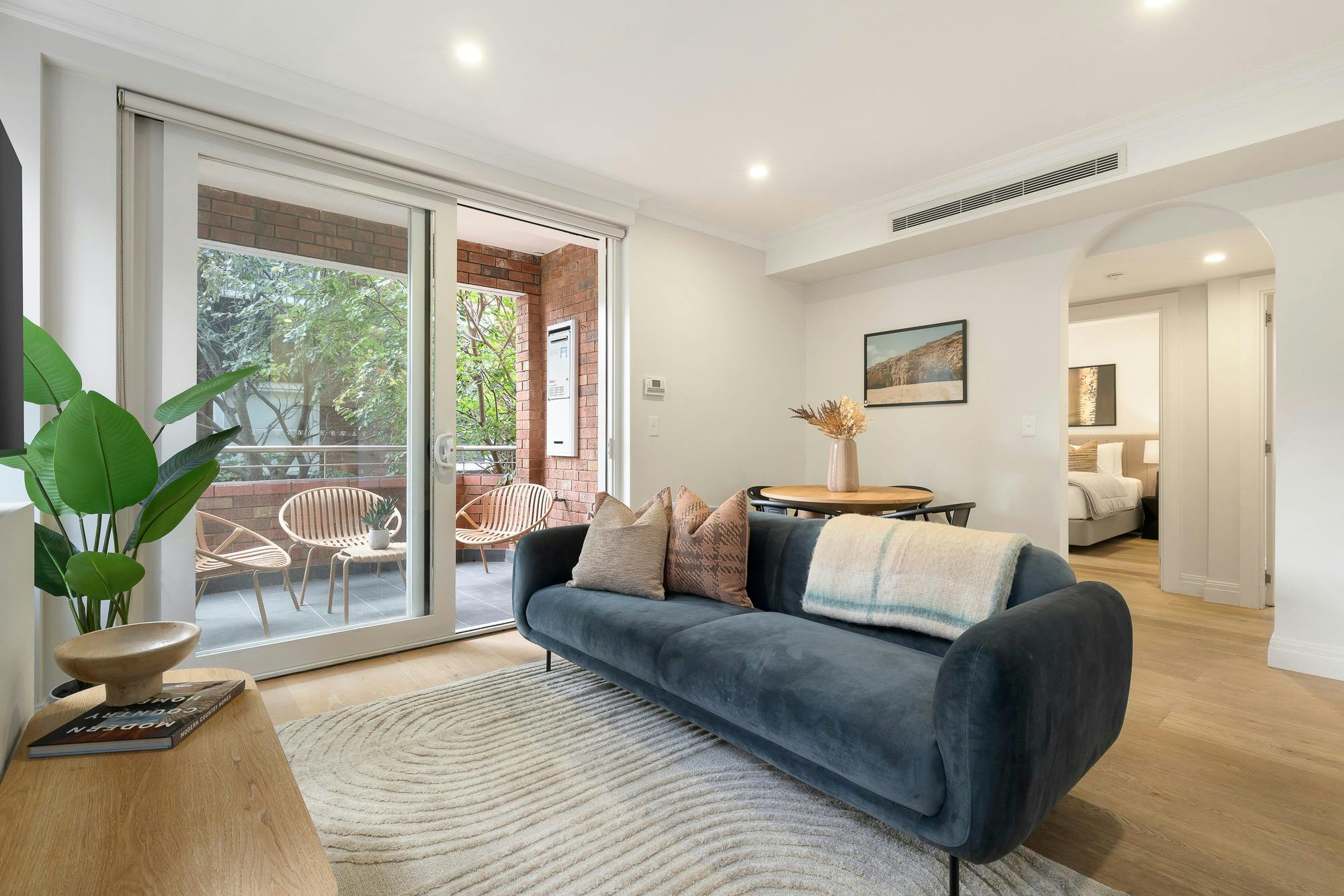 Spacious living room with large blue couch and dining set, leading out onto balcony with outdoor set
