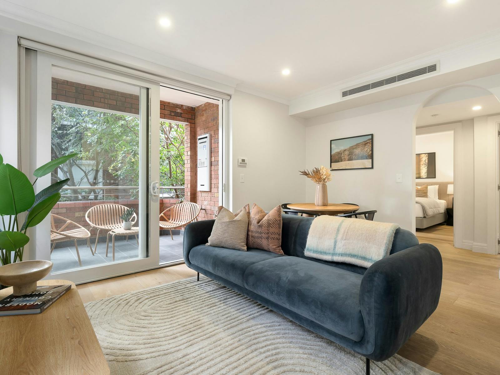 Spacious living room with large blue couch and dining set, leading out onto balcony with outdoor set