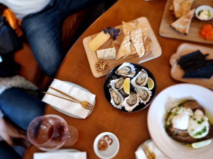 Birds eye view of lounge, wine glasses, cheese platter, oysters, burrata, placed on a low table