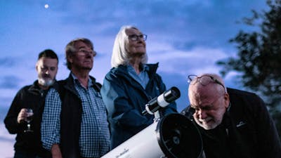 Man puts his eye to telescope to study the sky