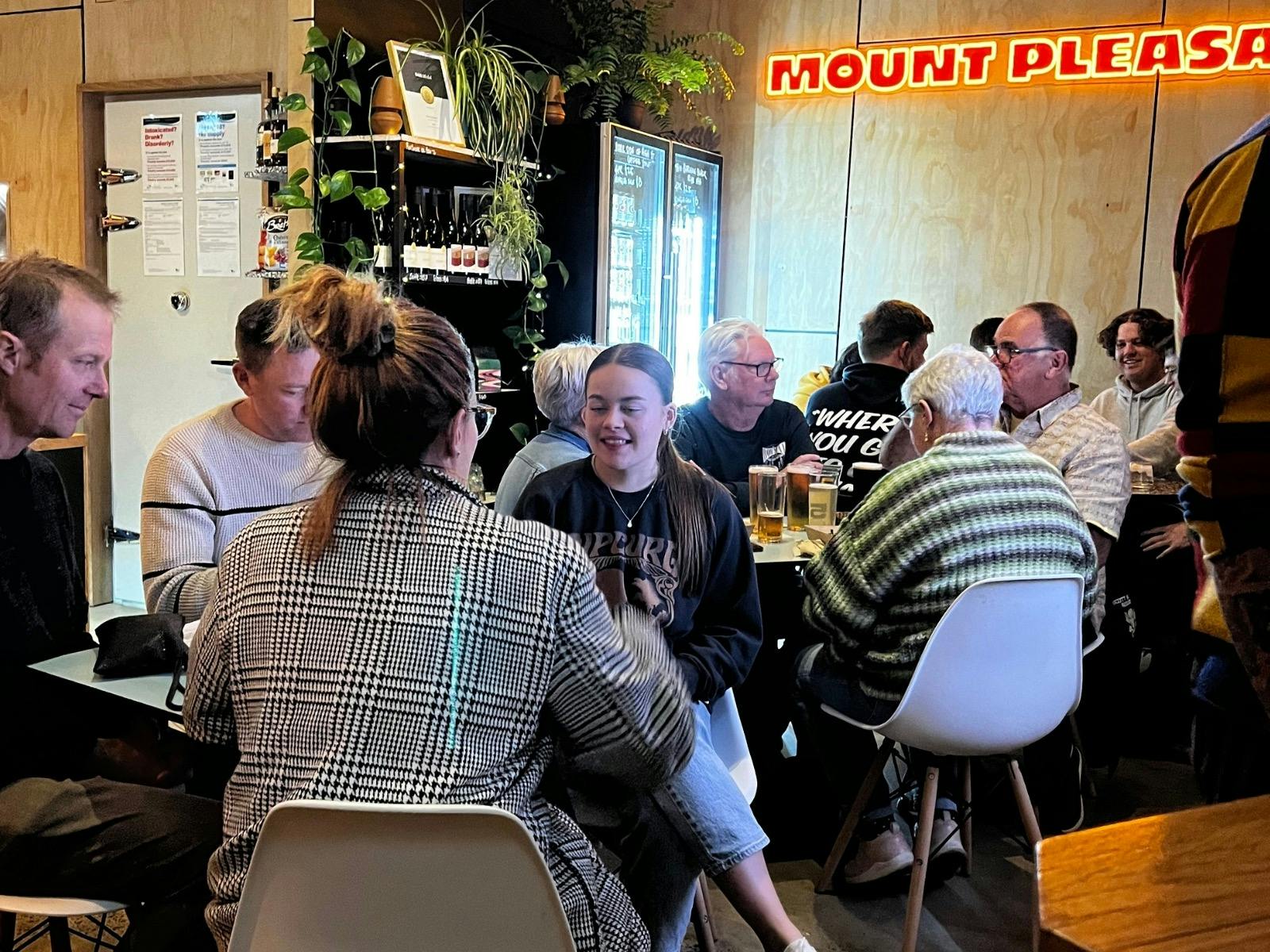 Group of people drinking inside the taproom with neon sign in background