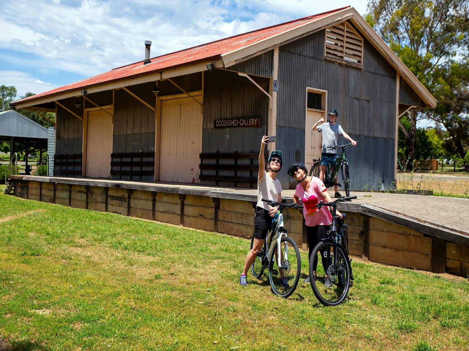 cyclists take a photo in front of a historic railway station along the Great Victorian Rail  Trail