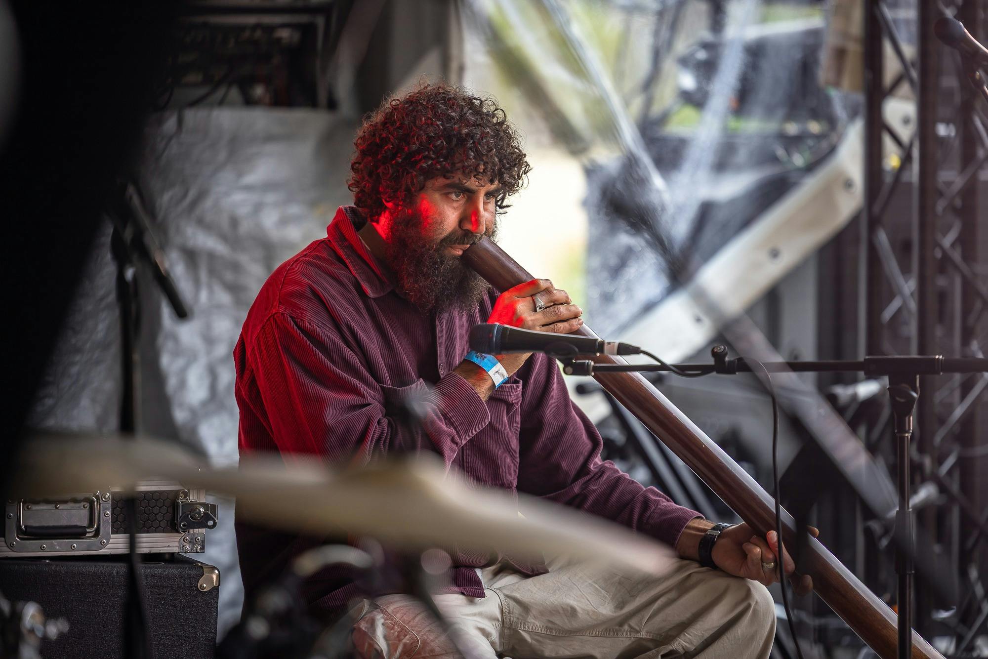An Aboriignal man wearing a maroom shirt plays didgeridoo on stage