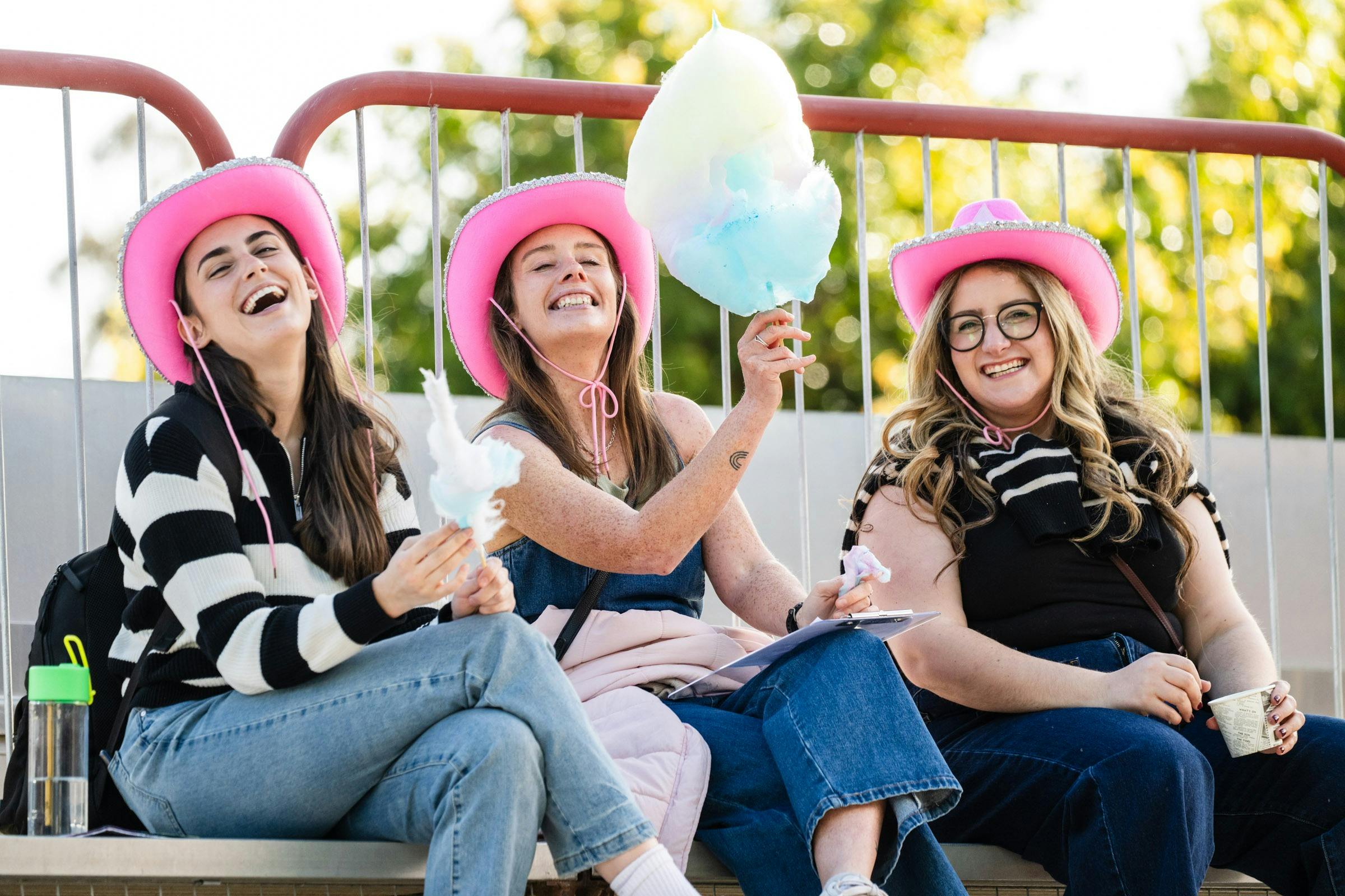 three friends wearing pink cowgirl hats holding fairy floss