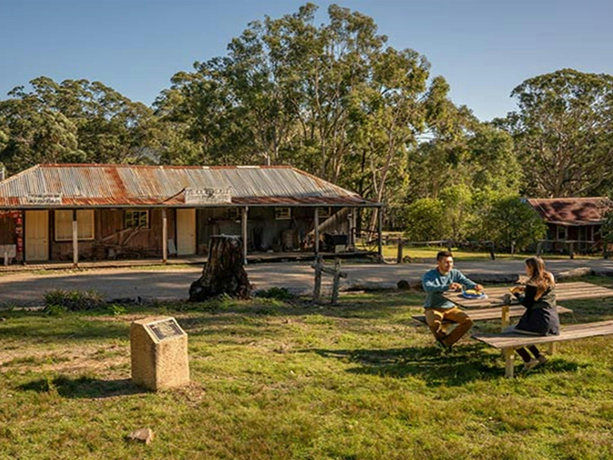Ein Paar genießt seinen Morgentee am Picknicktisch vor dem The Bank Room im Yerranderie Regional Park.