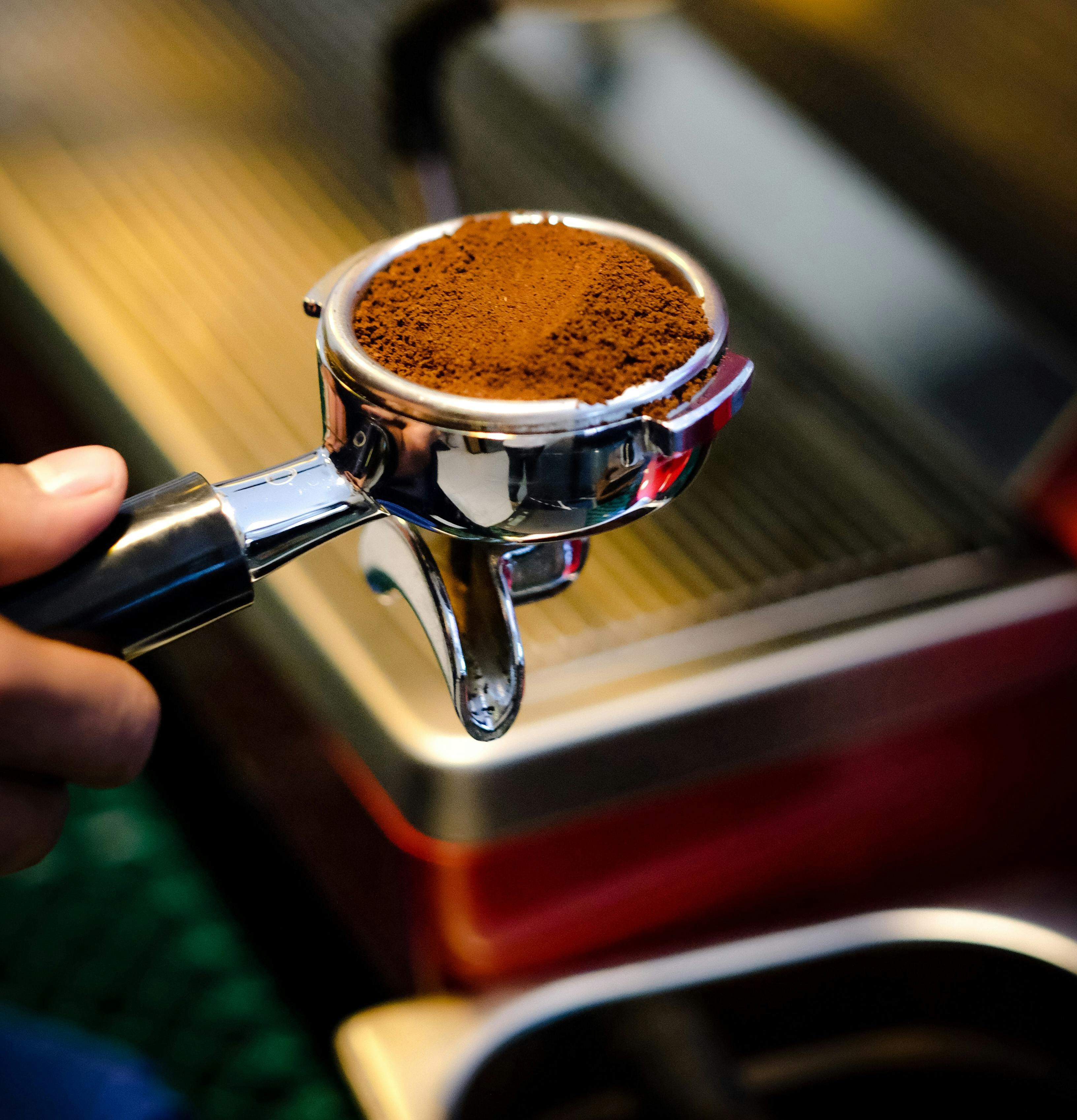 A barista holding a coffee grinder in front of a coffee machine