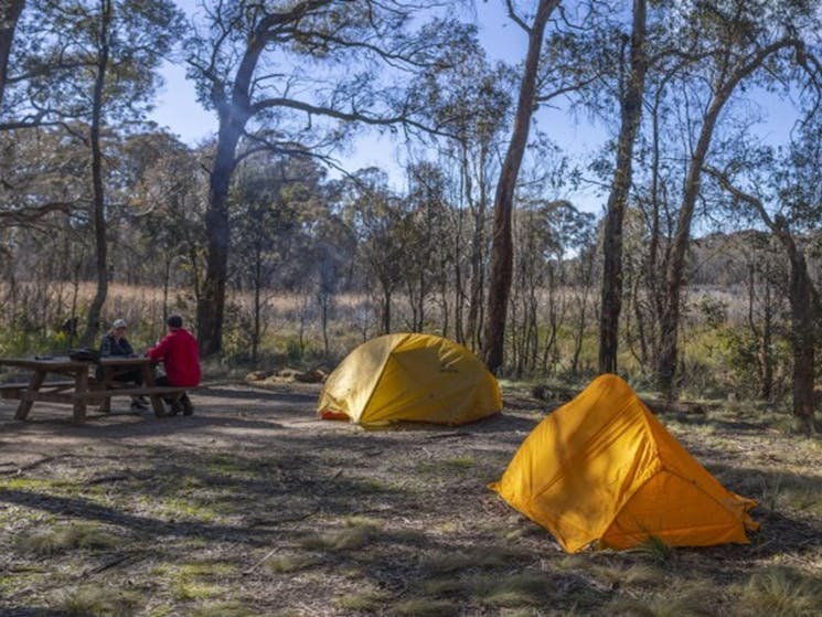 Two people sit at a picnic table with their tents in the foreground at Barokee campground, Cathedral
