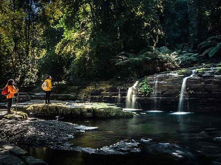 A man and woman stand by a creek waterfall along Rocky Crossing walking track in Barrington Tops.