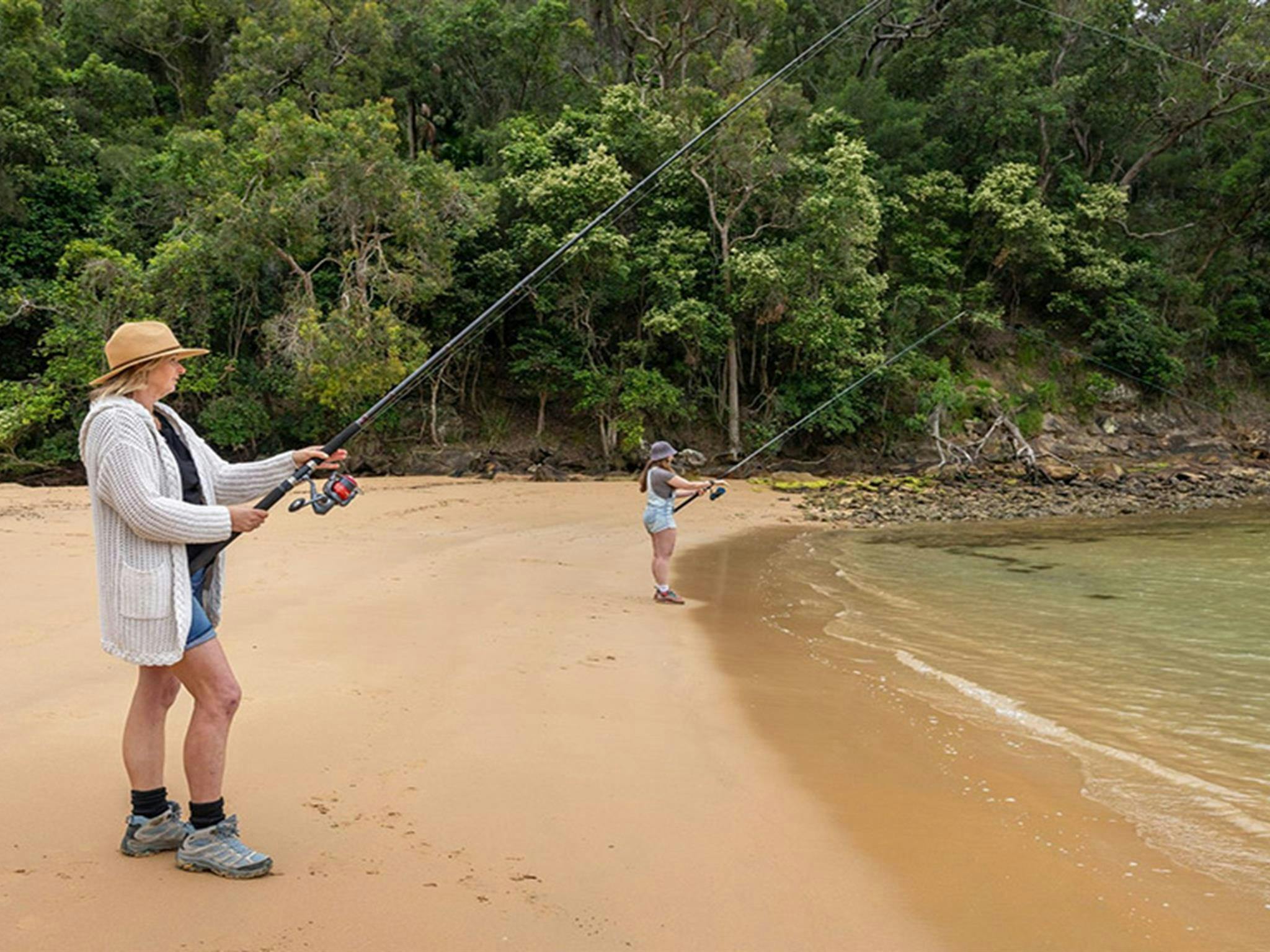 两人在盆地泻湖边垂钓，库灵盖蔡斯国家公园的绿树环绕其间。