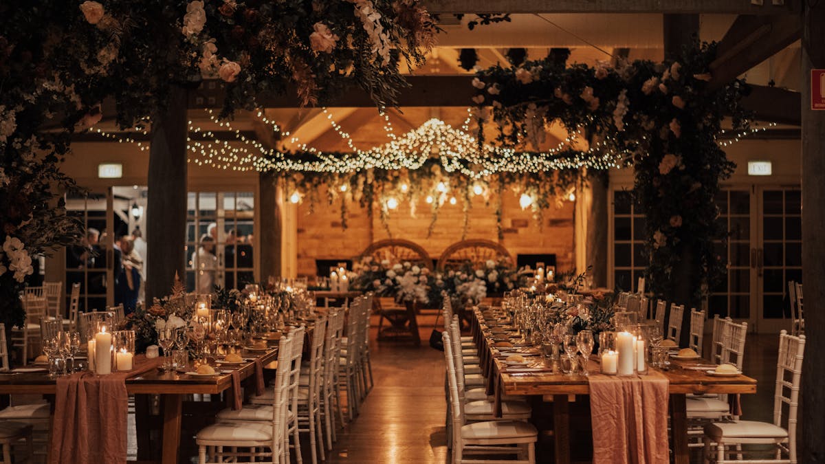 A wedding reception with fairylights in the ceiling, long timber tables and romantic candles.